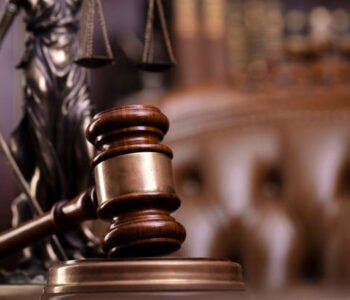 Judge’s gavel, Themis sculpture and collection of legal books on the brown background.